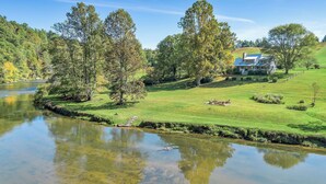 A riverside property with a house, a grassy lawn, and trees.
