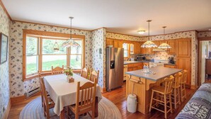 A kitchen with wooden cabinets, a stainless steel refrigerator, a dining table with chairs, and a large island with bar stools.