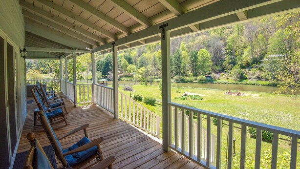 A covered porch with wooden benches and a view of a lush garden and river.