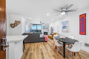A modern living room with a sofa, dining table, and chairs. There is a fireplace and a ceiling fan.