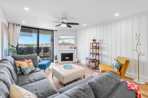 A modern living room with a fireplace, a ceiling fan, and a view of the city.