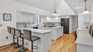 A modern kitchen with white cabinetry, a central island, bar stools, a black refrigerator, and a chandelier. - Cheerful 6-Bedroom Villa with Pool and Tennis Courts near the beach! (Fairfield)
