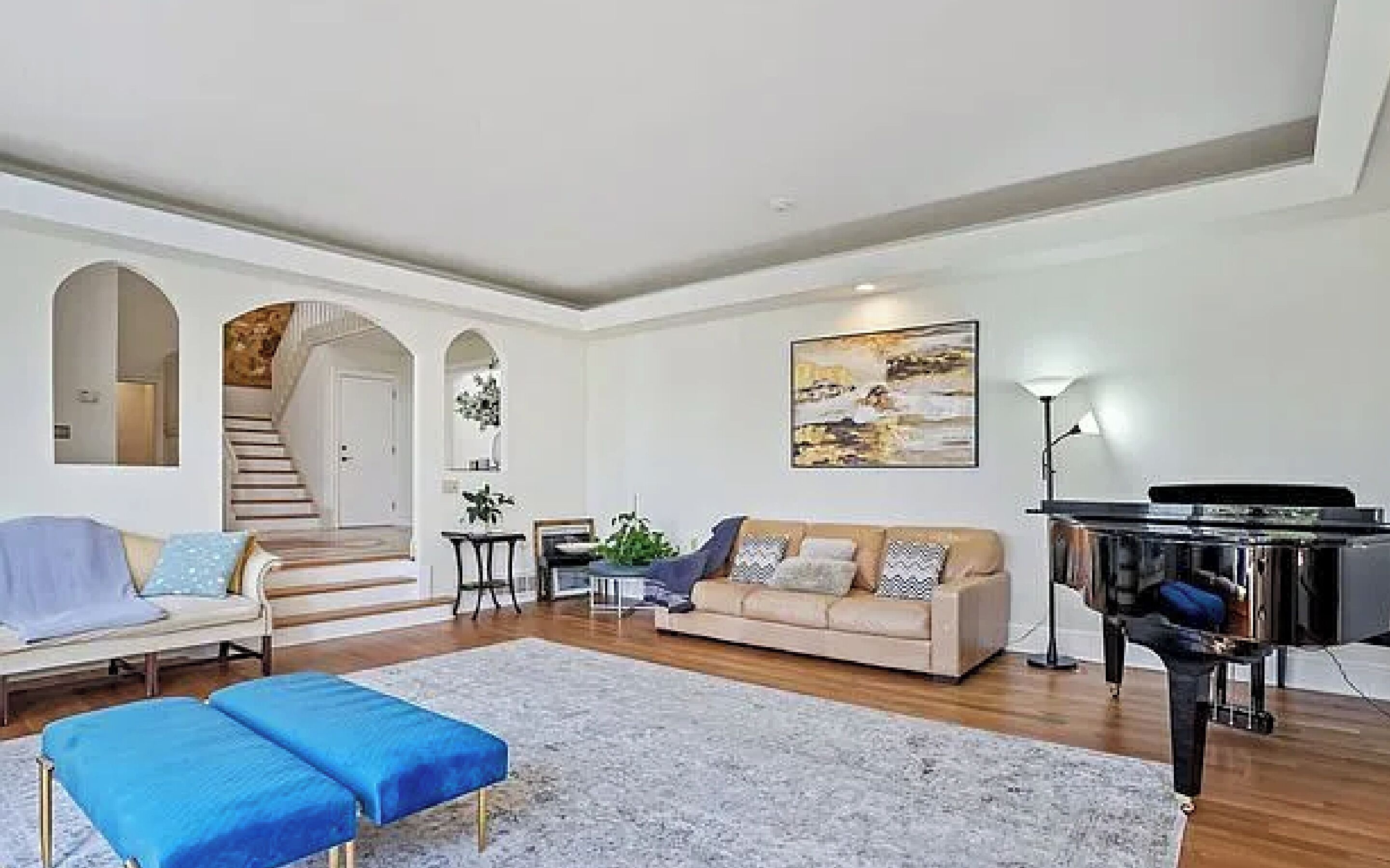 Un salon spacieux comprenant un canapé, un banc bleu, un piano et un escalier menant à une autre pièce.