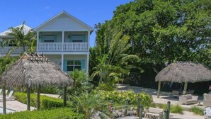 A poolside area with lounge chairs, a thatched-roof structure, and a building in the background. - Isla Key Acaí: Waterfront Boutique Resort, FREE Boat Dockage Sep-Oct Only! (Islamorada)