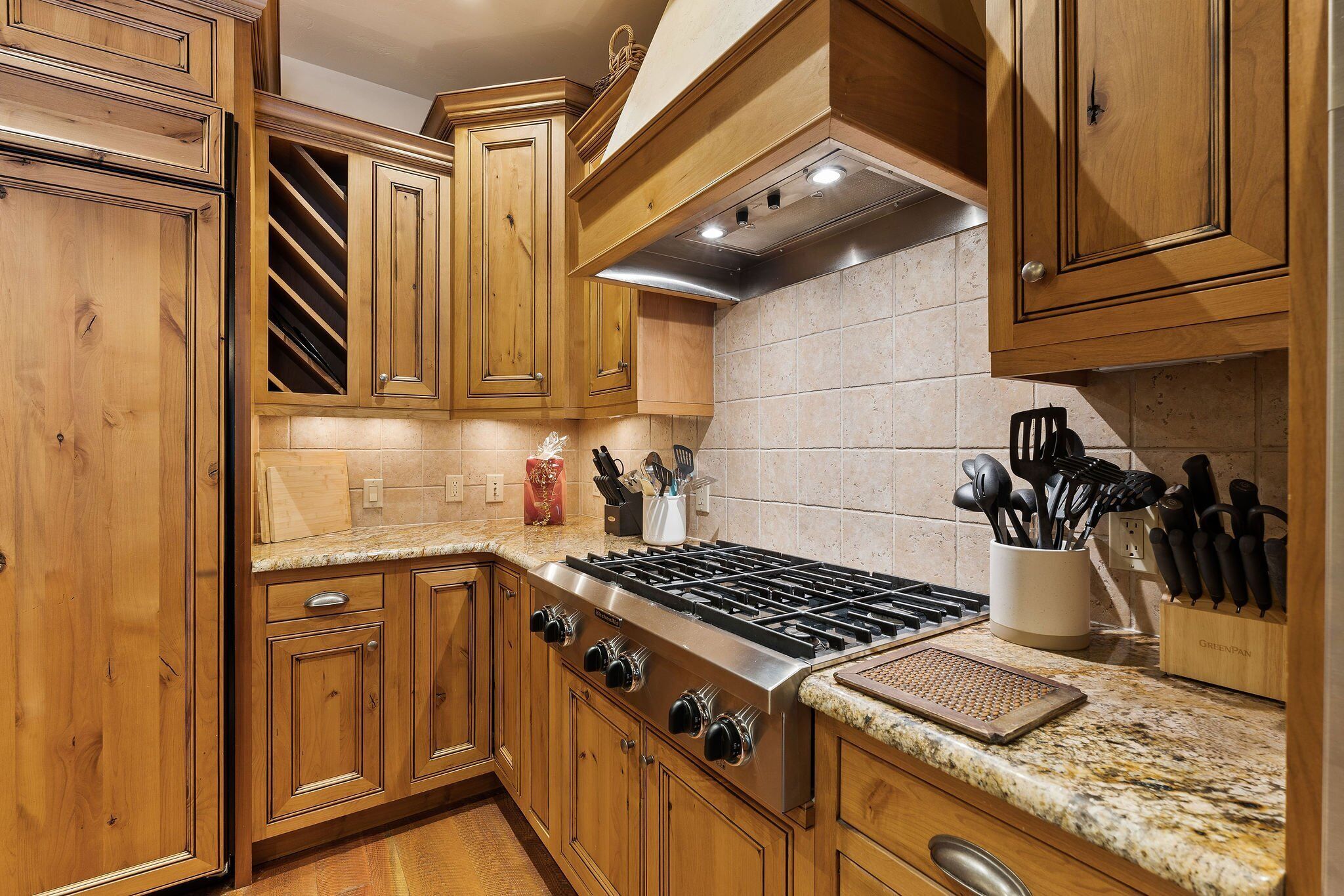 A kitchen with wooden cabinets, a stainless steel stove, granite countertops, and a range hood.