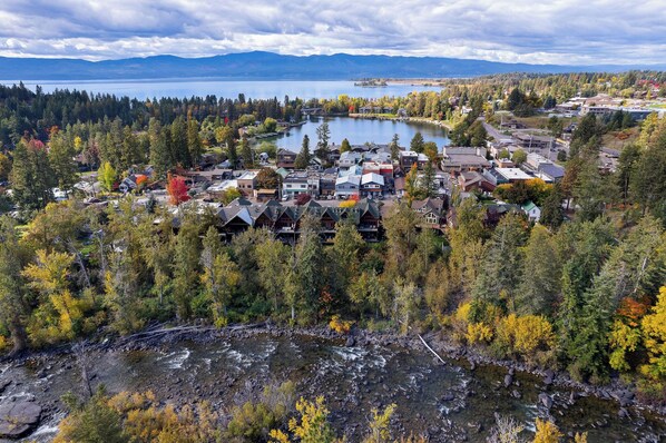 A lakeside town with a river, dense forest, and mountains in the background.