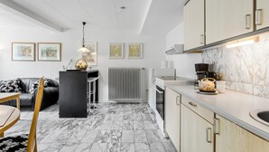 Et moderne køkken med marmorgulv, et spiseområde med en sort lædersofa og en barstol i sort.