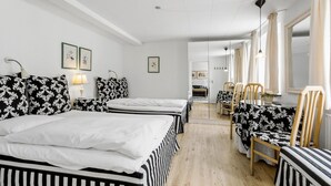 Et hotelværelse med to senge, et spiseområde med stole og et bord, samt et køkken i baggrunden.