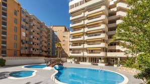 A swimming pool area with multiple pools and a bridge, surrounded by apartment buildings.