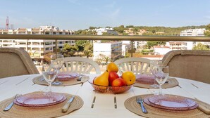 A table set for two with a fruit bowl, wine glasses, and plates on a balcony overlooking a cityscape.