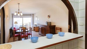 A compact kitchen with a central island, a dining area with chairs and a table, and a view through an archway to a balcony.