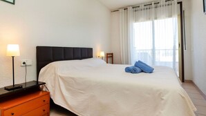 A bedroom with a bed, a nightstand, a lamp, a ceiling fan, and a window with curtains.