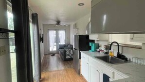 A narrow, open-plan kitchen and living area with wooden flooring, a ceiling fan, and a view to the outside. - EL948 (Canyon Lake)