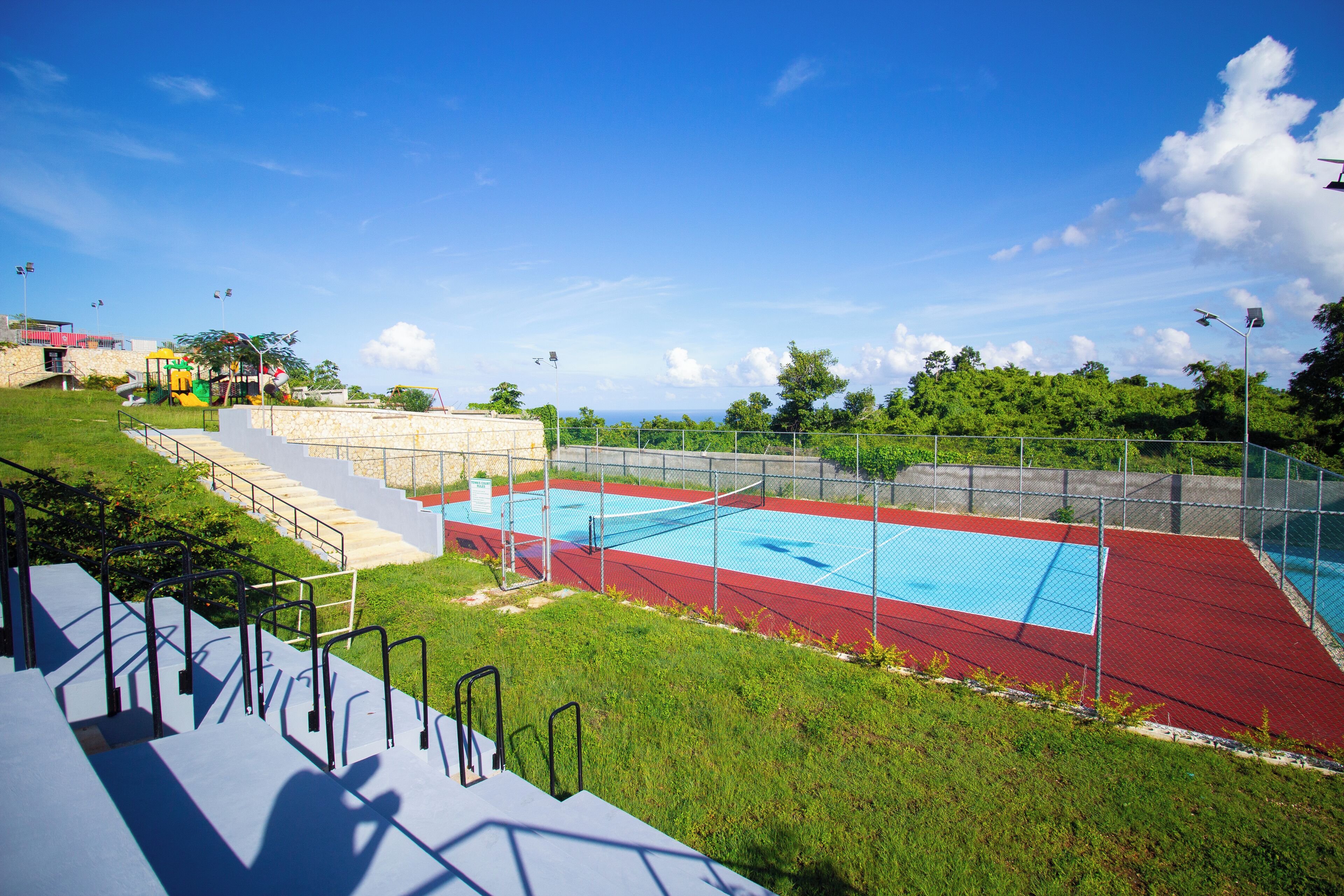 A swimming pool with a red and blue deck, surrounded by a fence, and a set of stairs leading up to it.
