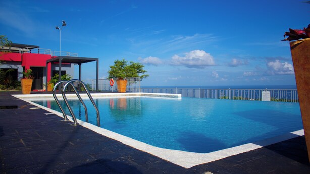 A swimming pool with a metal ladder, surrounded by a white pool edge, with a view of the ocean and a red building in the background. - D&D Divine Suite
Ocho Rios, St. Ann Parish (Ocho Rios)