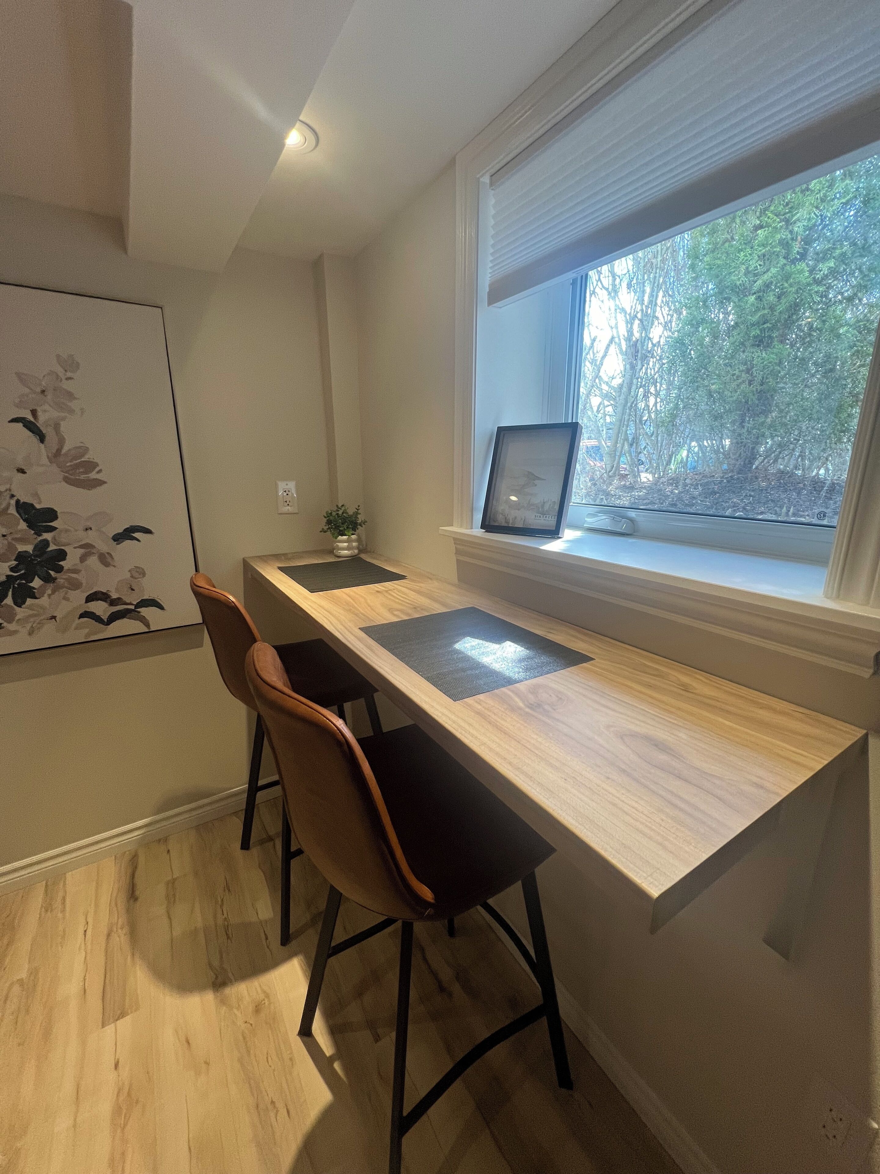 Un espace de travail moderne avec un bureau en bois, deux chaises, un ordinateur portable et une fenêtre donnant sur des arbres.