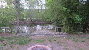 A wooden deck with chairs, a fire pit, and a pond.