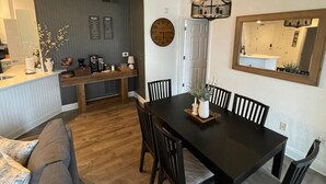 Une cuisine moderne avec un îlot central en bois, un coin repas avec une table et des chaises en bois foncé, et un grand miroir au mur.