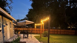 A paved patio with a wooden fence, outdoor furniture, and string lights. - Beautiful Family-sized Home in Sunny Sarasota, Florida with large backyard! (Sarasota)