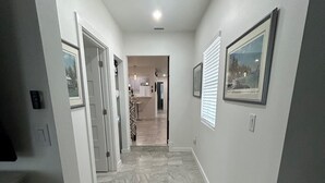 A hallway with a tiled floor, white walls, and framed pictures on the walls. - Beautiful Family-sized Home in Sunny Sarasota, Florida with large backyard! (Sarasota)