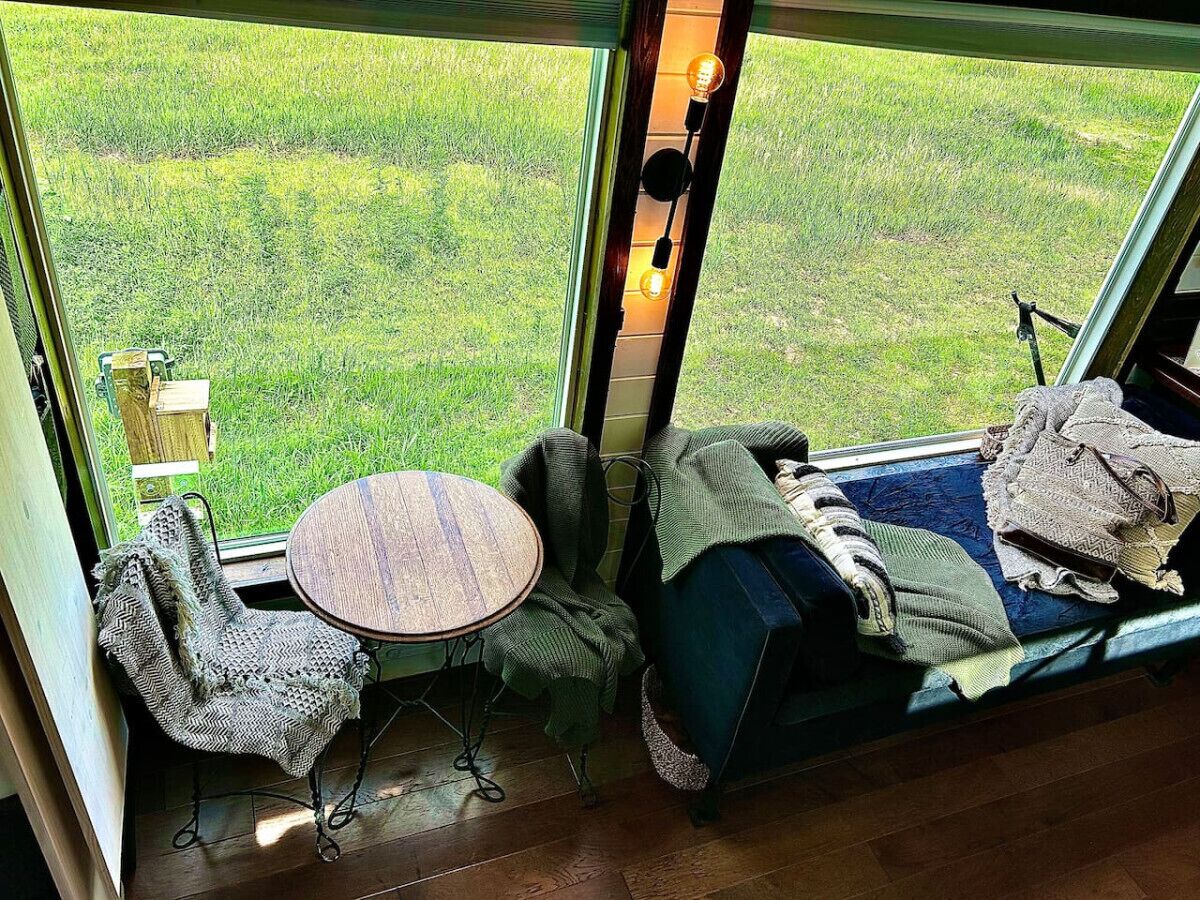 Una habitación acogedora con un ventanal grande, una mesa redonda, una silla y una cama con mantas.