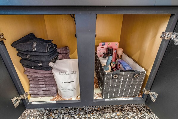 A storage area with neatly folded towels, a hand soap refill, and a hair dryer kit.