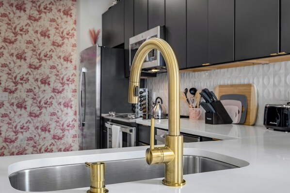 A kitchen with a modern stainless steel sink and a gold faucet.