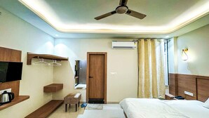 A hotel room with a bed, a ceiling fan, a TV, a wardrobe, a mirror, a shelf, and a window with curtains. - Hotel Neel Kamal (Jaipur)