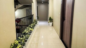 A hallway with a tiled floor, a staircase on the left, a door on the right, and a row of potted plants along the wall. - Hotel Neel Kamal (Jaipur)