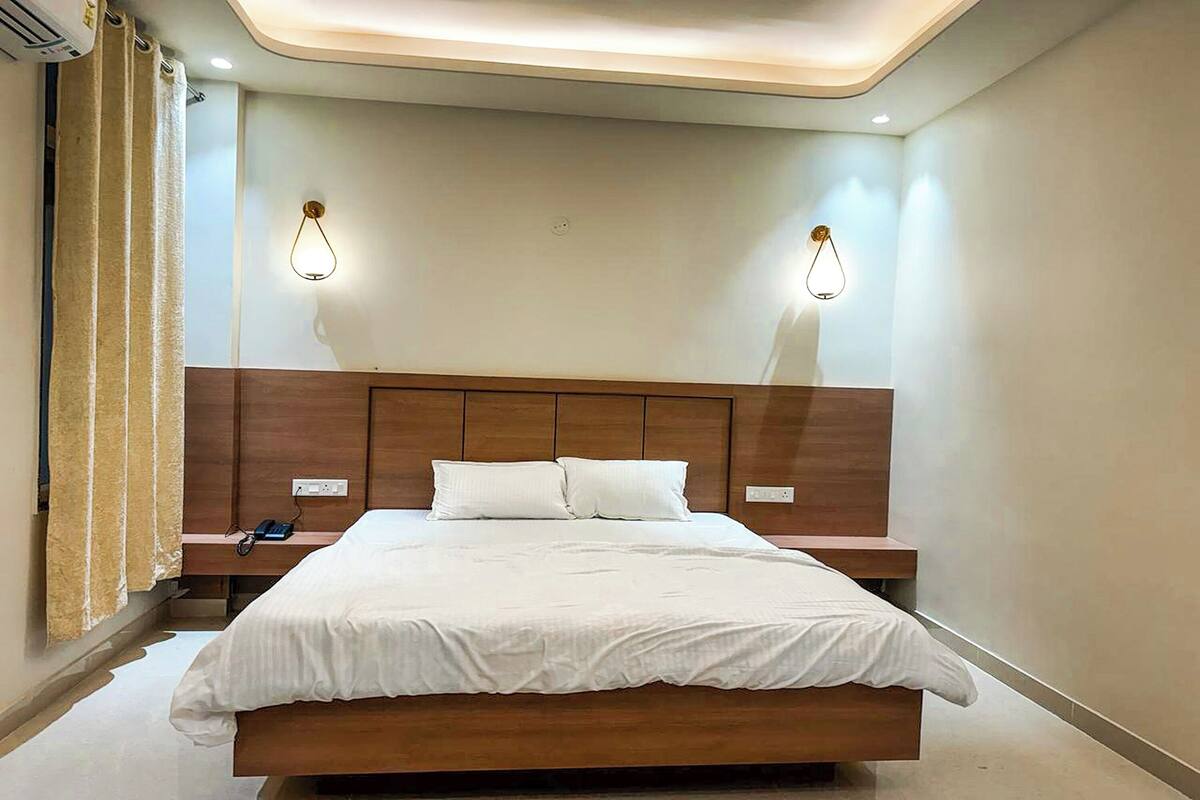 Een moderne hotelkamer met een groot bed, een houten hoofdbord, twee nachtkastjes en wandlampen.