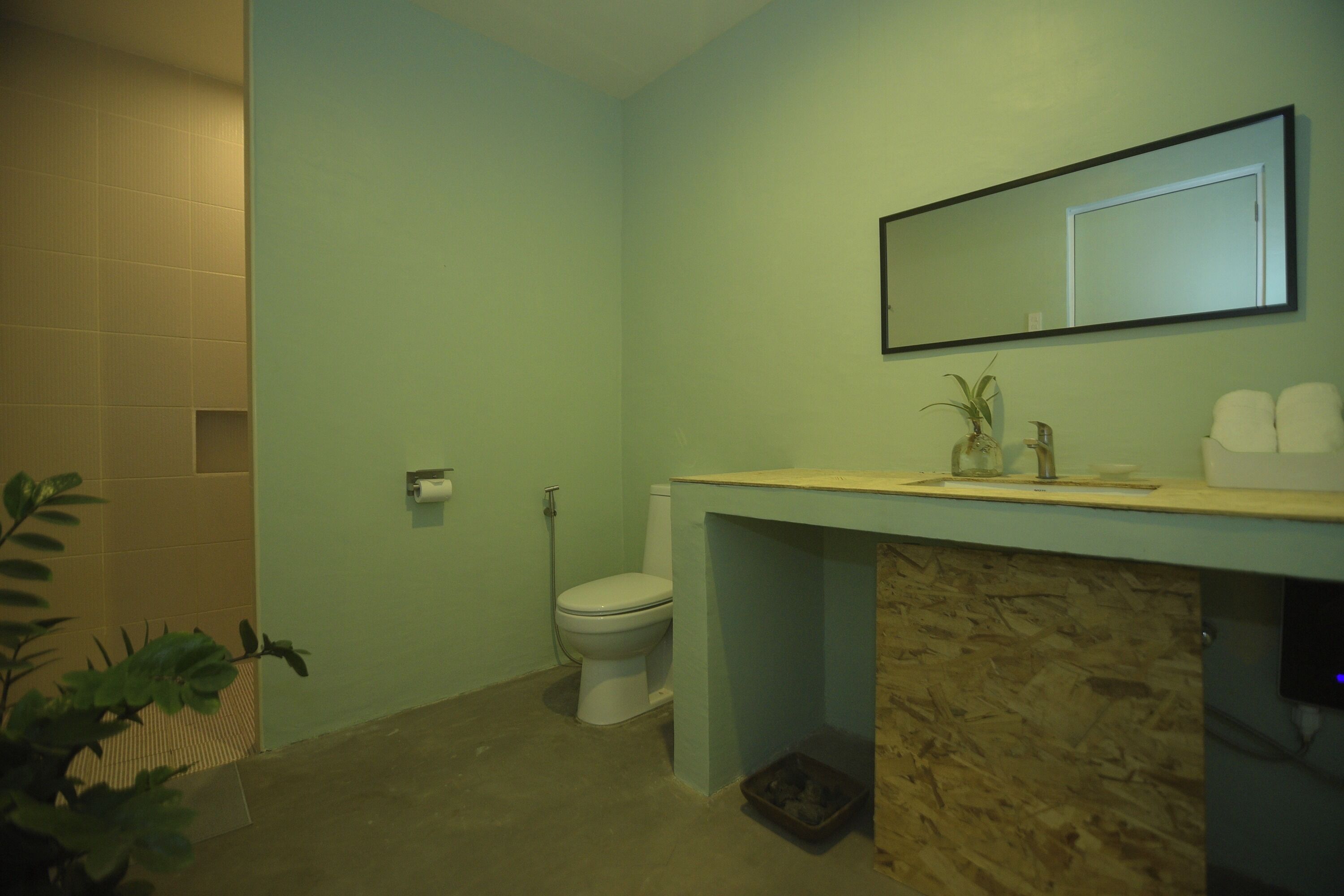 A bathroom with a toilet, sink, mirror, and a plant.