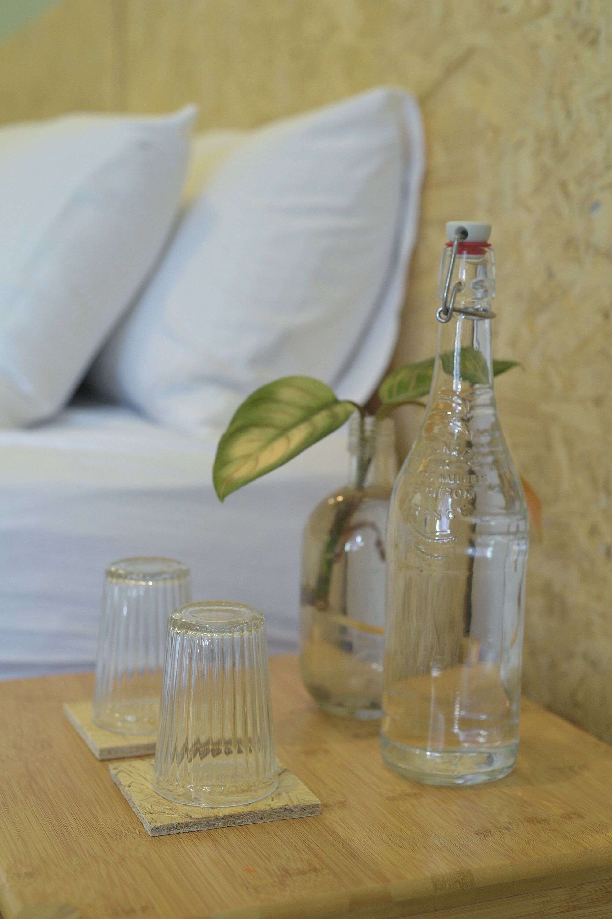 Una mesa de madera con dos botellas de vidrio transparente y dos vasos sobre posavasos.
