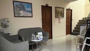A hotel lobby with a grey sofa, a small table with a brochure, a staircase, and a door. - One World One Home Patong 1 (Patong)