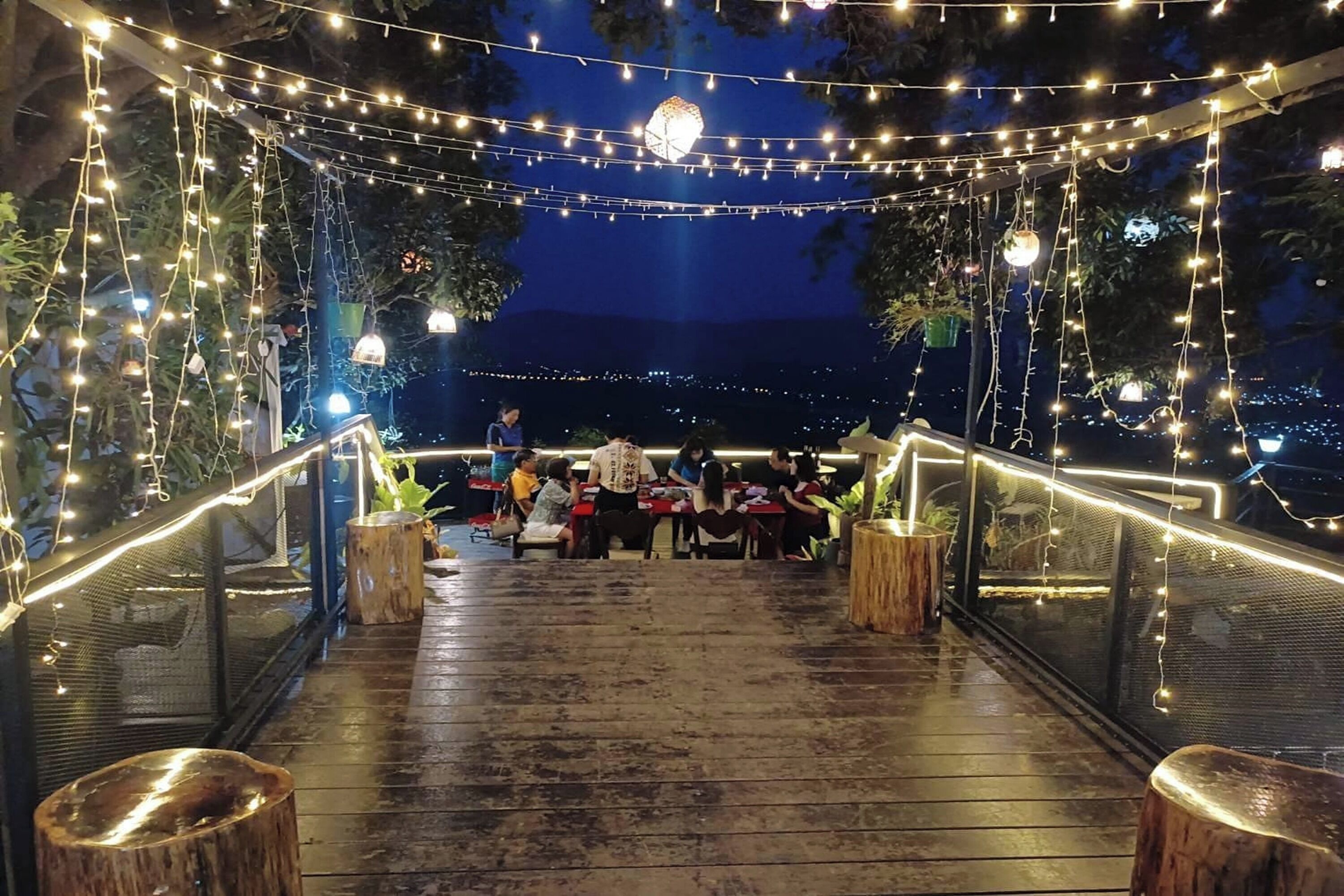 An outdoor dining area with string lights, wooden tables, and chairs.