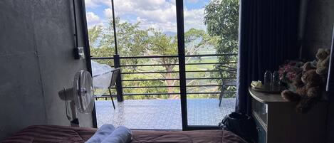 Une chambre avec un lit, un ventilateur, une commode et une vue sur la verdure.