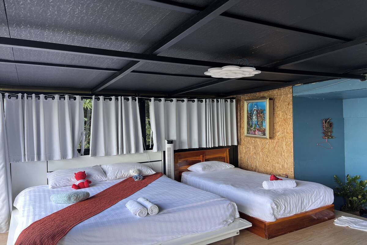 Een hotelkamer met twee bedden, witte beddengoed, een rode deken en een plafondventilator.