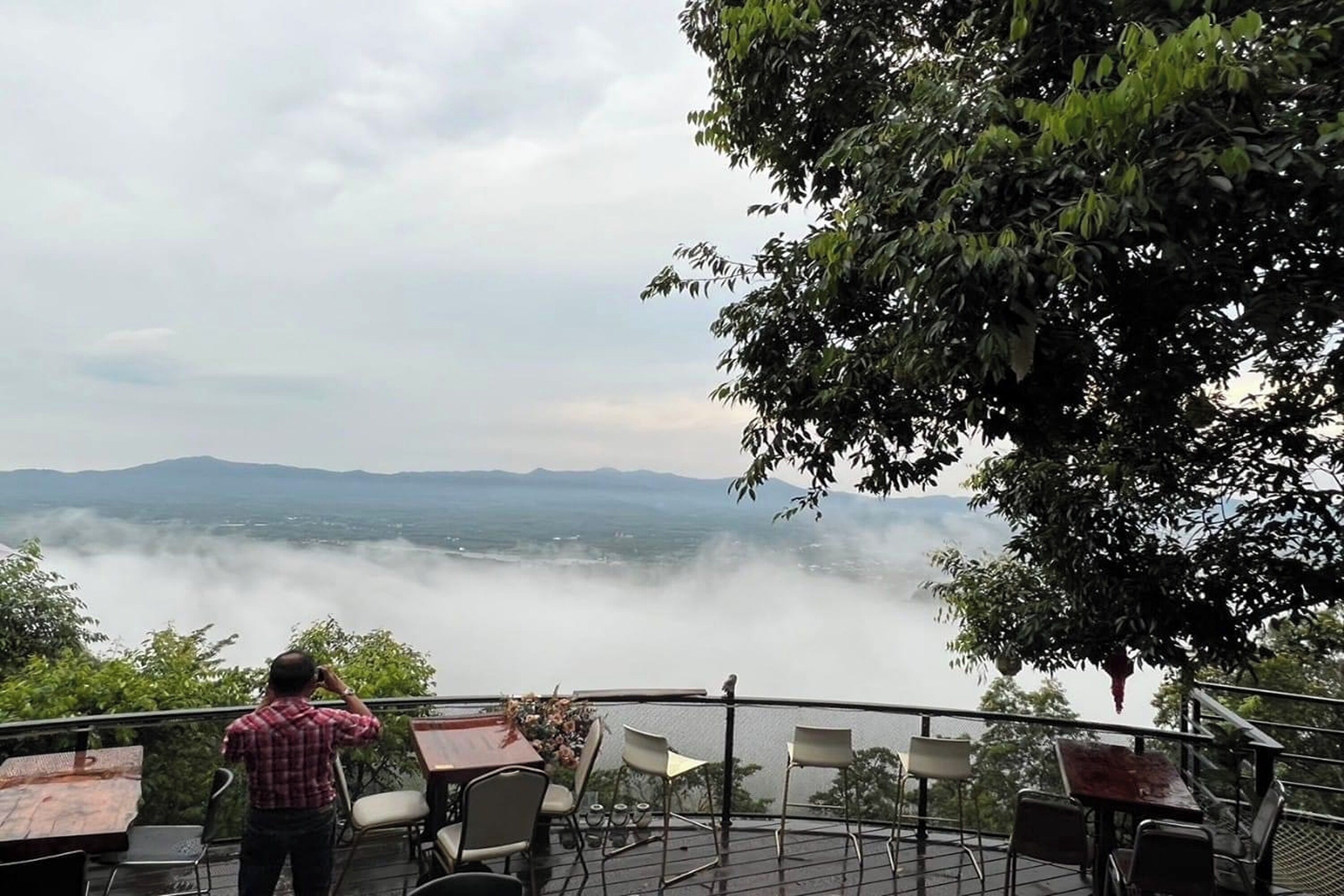 A terrace with tables and chairs overlooking a valley with mountains in the distance.