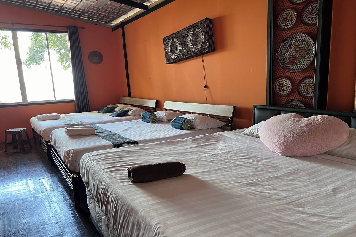Een hotelkamer met drie bedden, een groot raam, een decoratief wandpaneel en een plafondventilator.