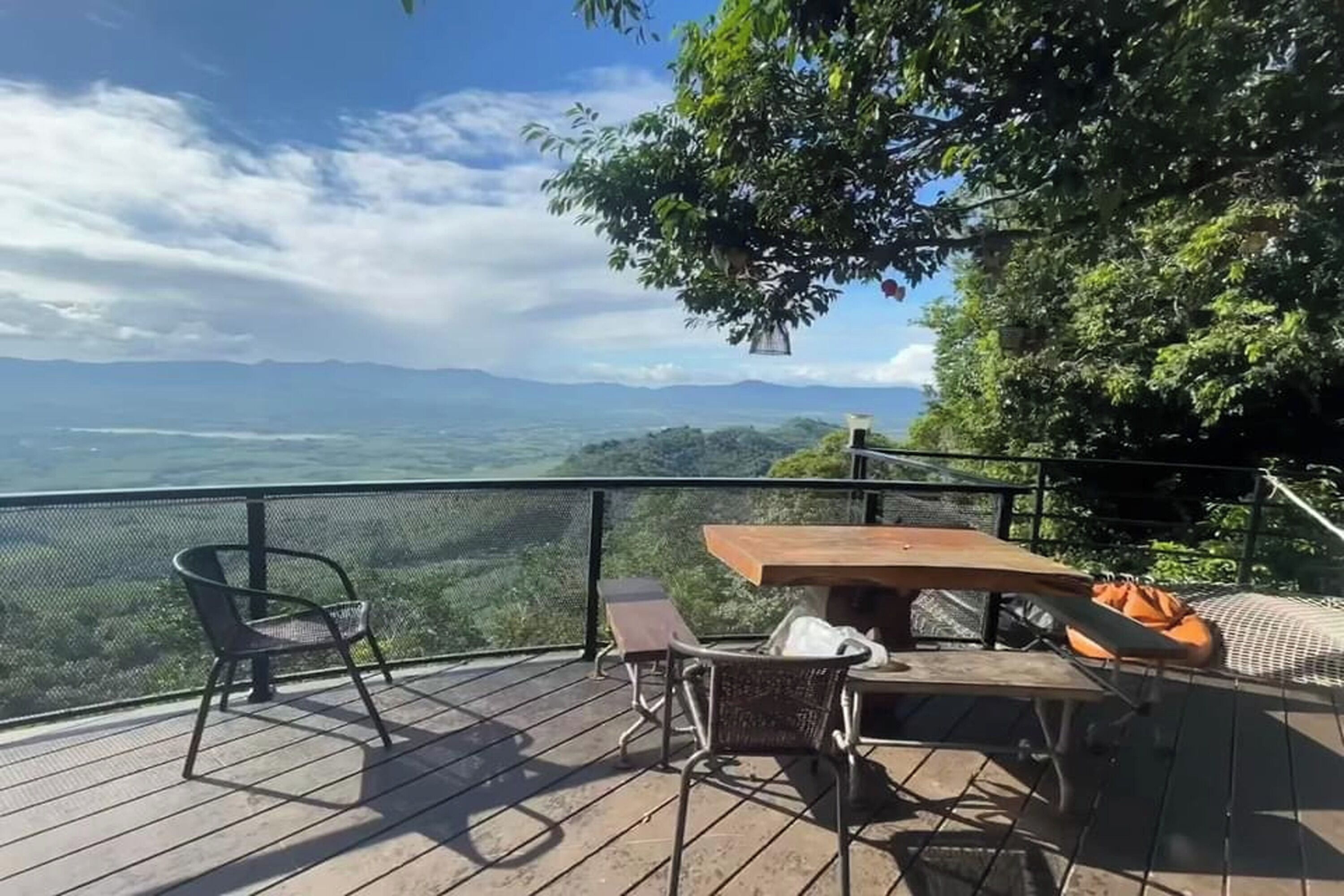 A wooden deck with a table and chairs, overlooking a scenic landscape with mountains and greenery.