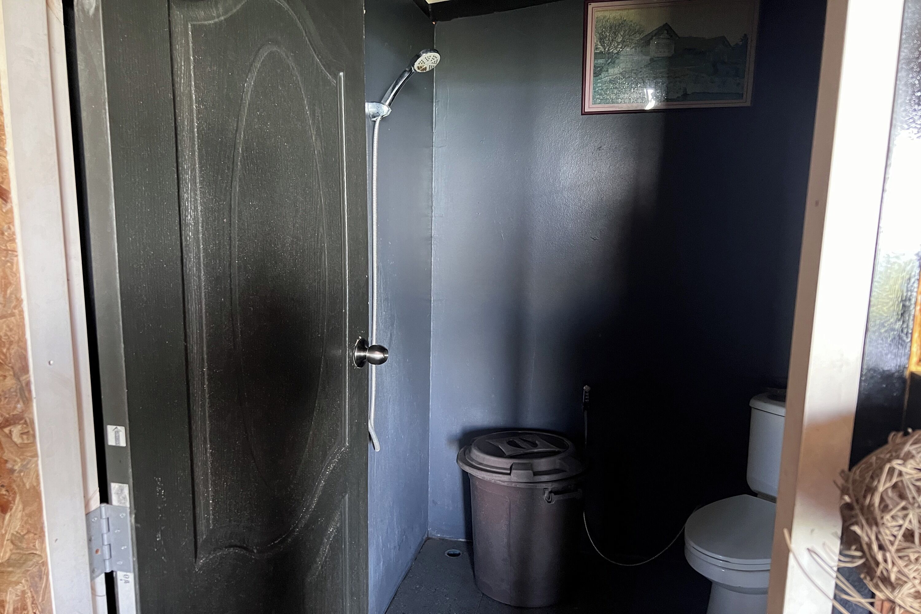 Un baño pequeño y oscuro con ducha, inodoro y cubo de basura.
