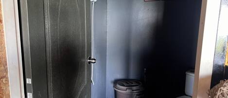 Un baño pequeño y oscuro con ducha, inodoro y cubo de basura.