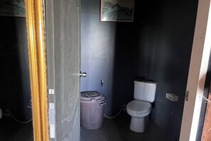 A small, dark-colored bathroom with a toilet and a trash bin. - Kuan Khan Lao The Nine Bistro (Na Mom)