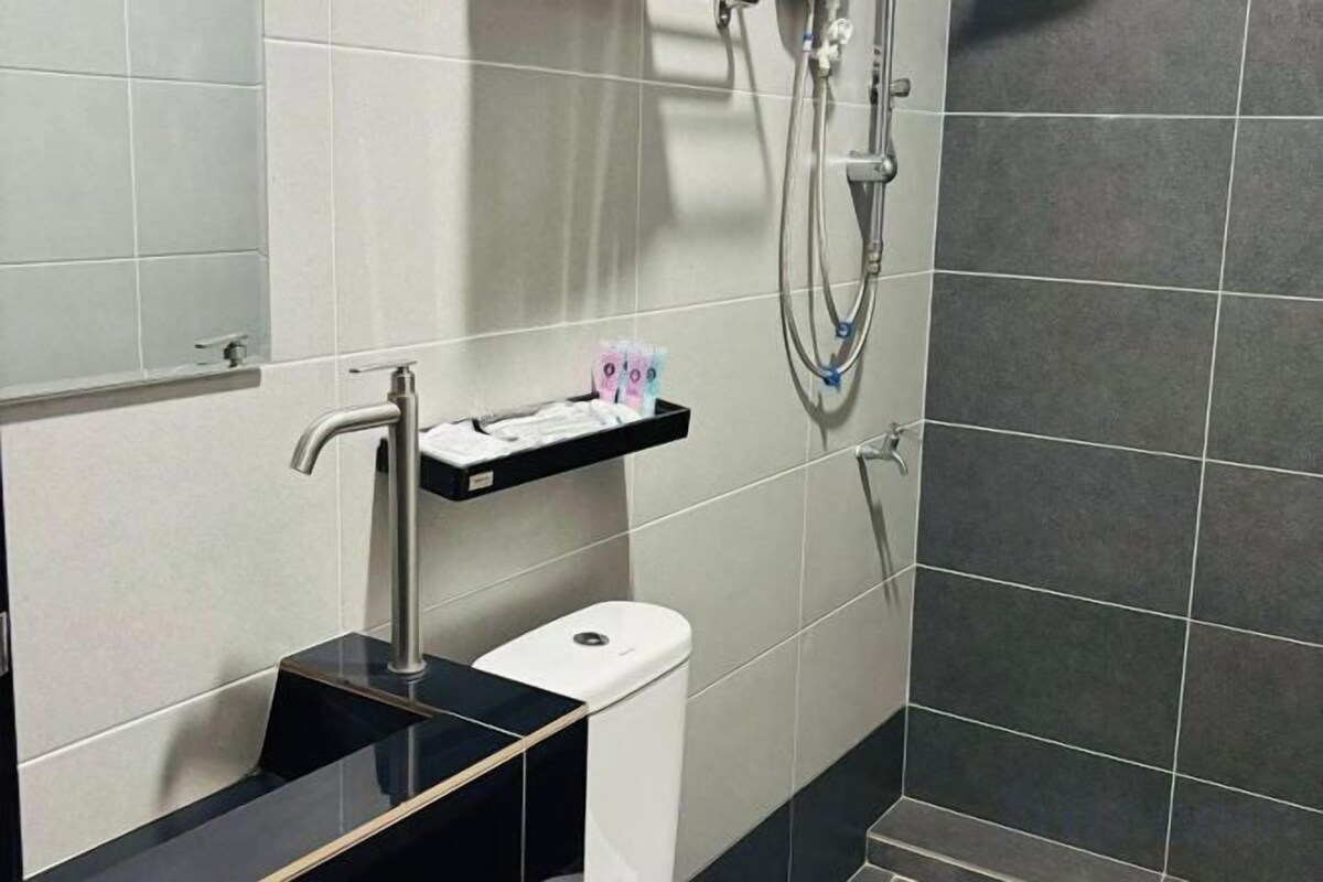 A bathroom with a toilet, a sink with a black countertop, and a shower area with a handheld showerhead.