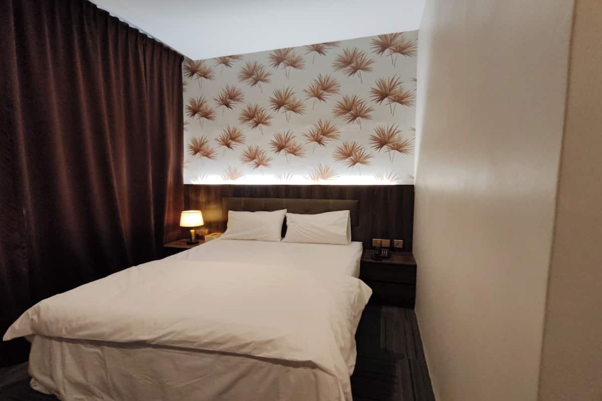 Una habitación de hotel con una cama grande, una mesita de noche con lámpara y una pared con estampado floral.
