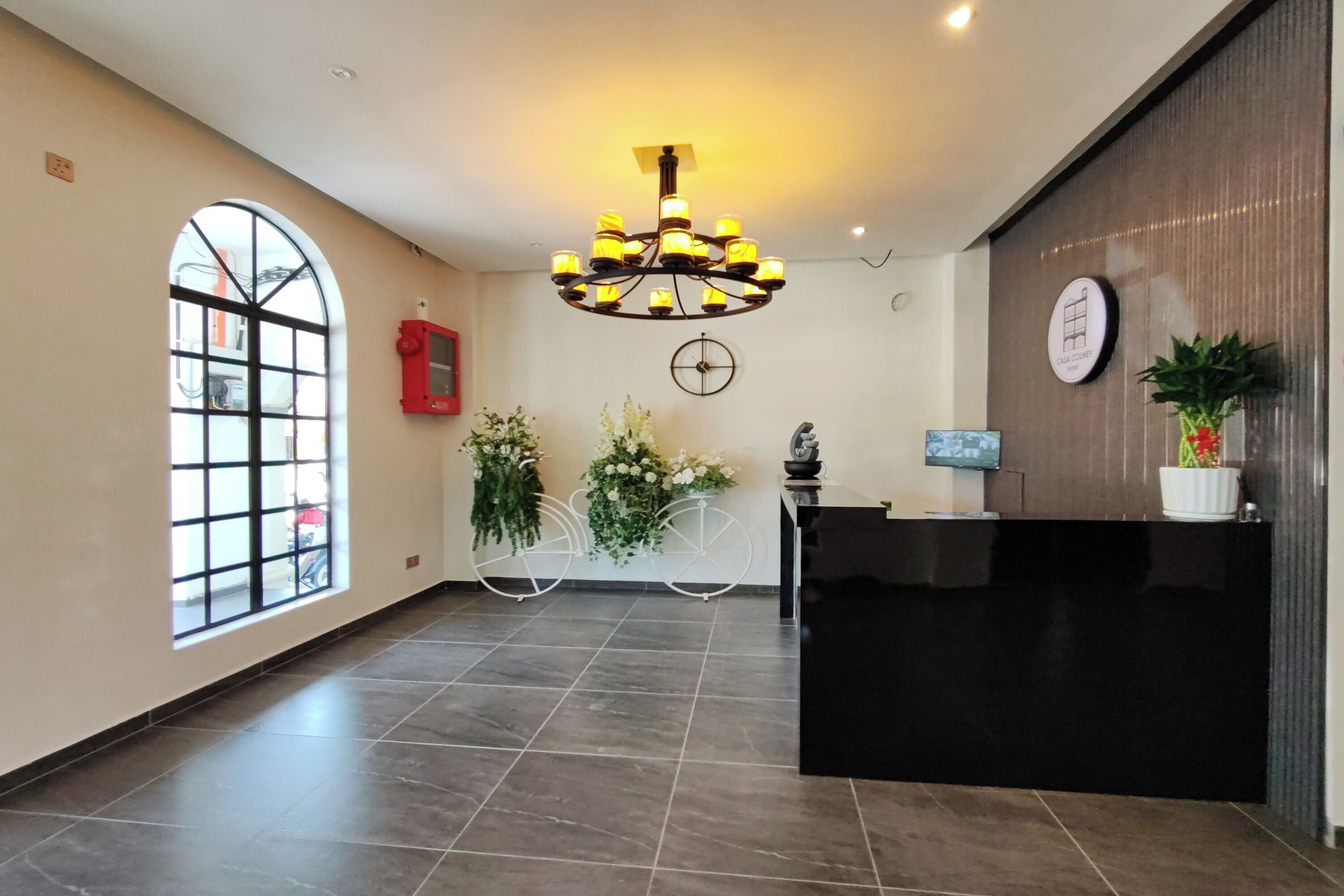 A reception area with a black reception desk, a large chandelier, a clock, and a window with a view of the outside.