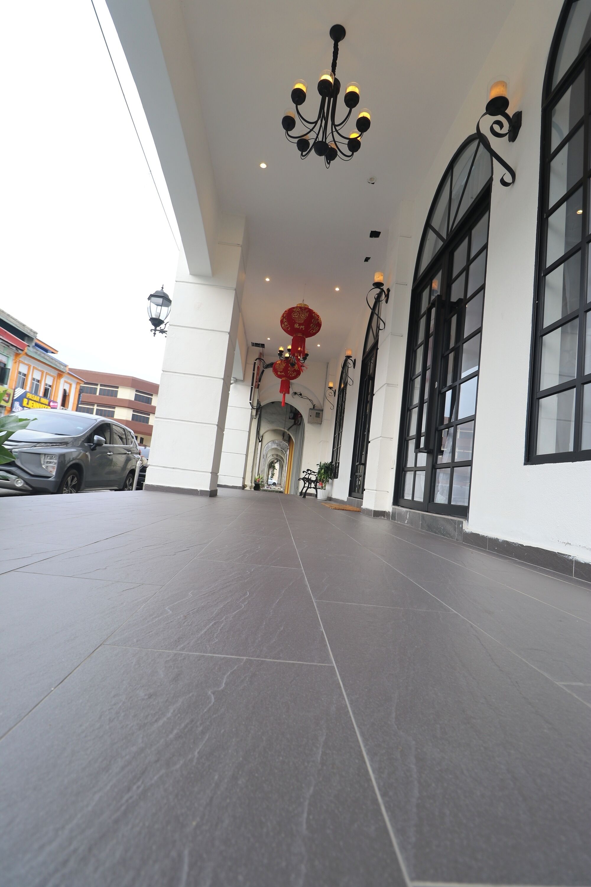 A spacious, well-lit hallway with a modern chandelier, large windows, and a tiled floor.