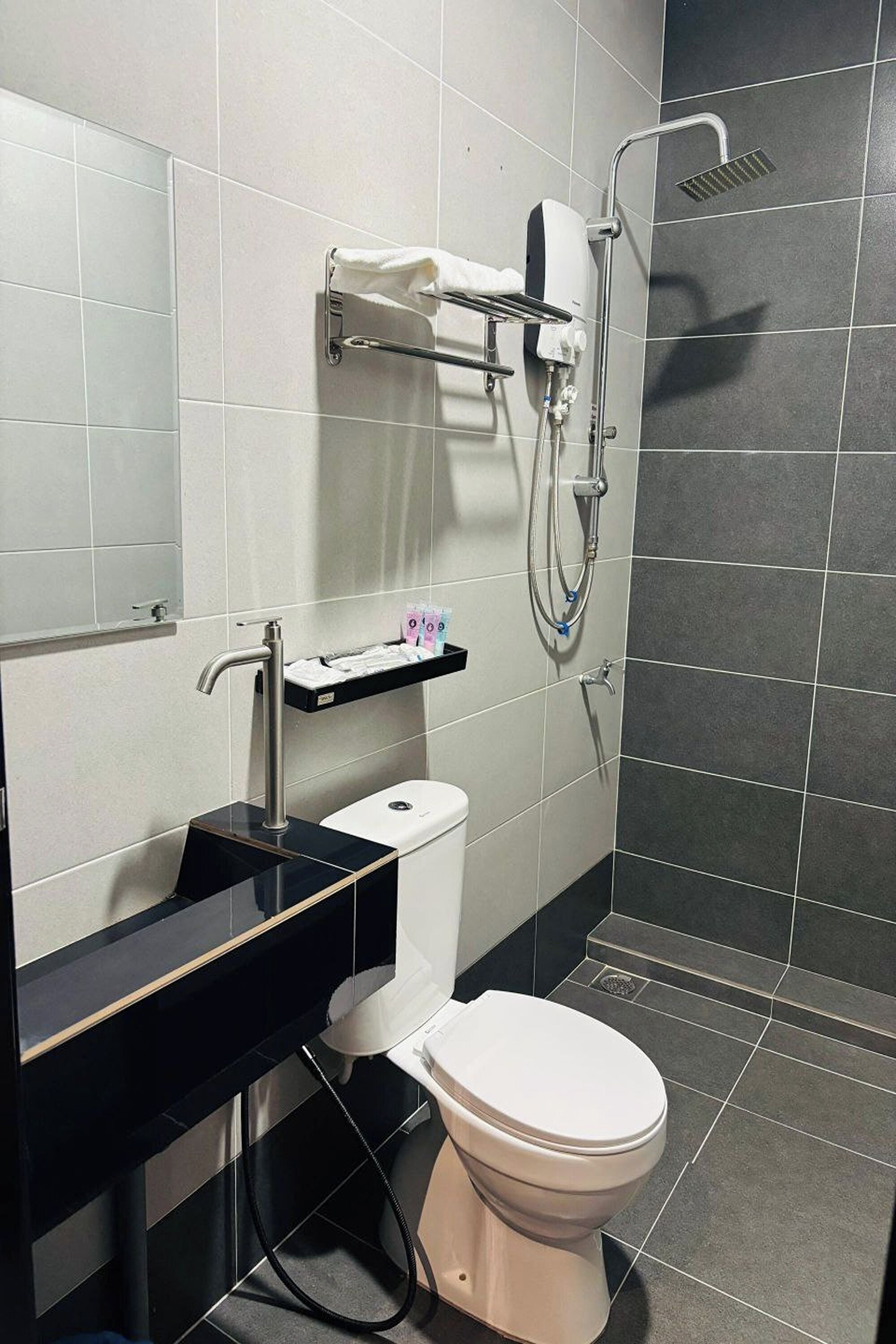 Un bany modern amb un lavabo negre, vàter blanc i zona de dutxa.