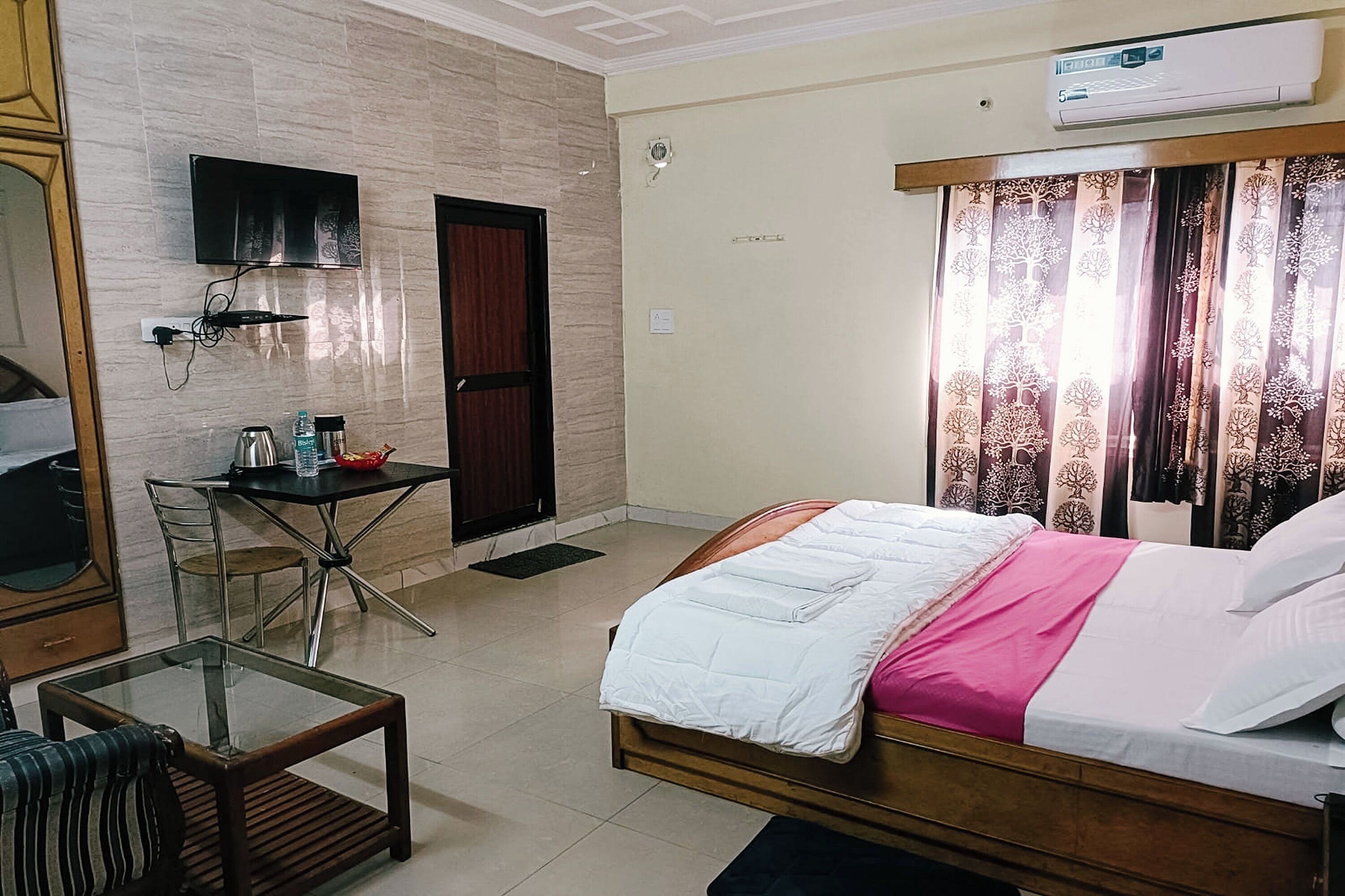 Habitación de hotel con cama, escritorio con silla, televisor montado en la pared y una puerta.