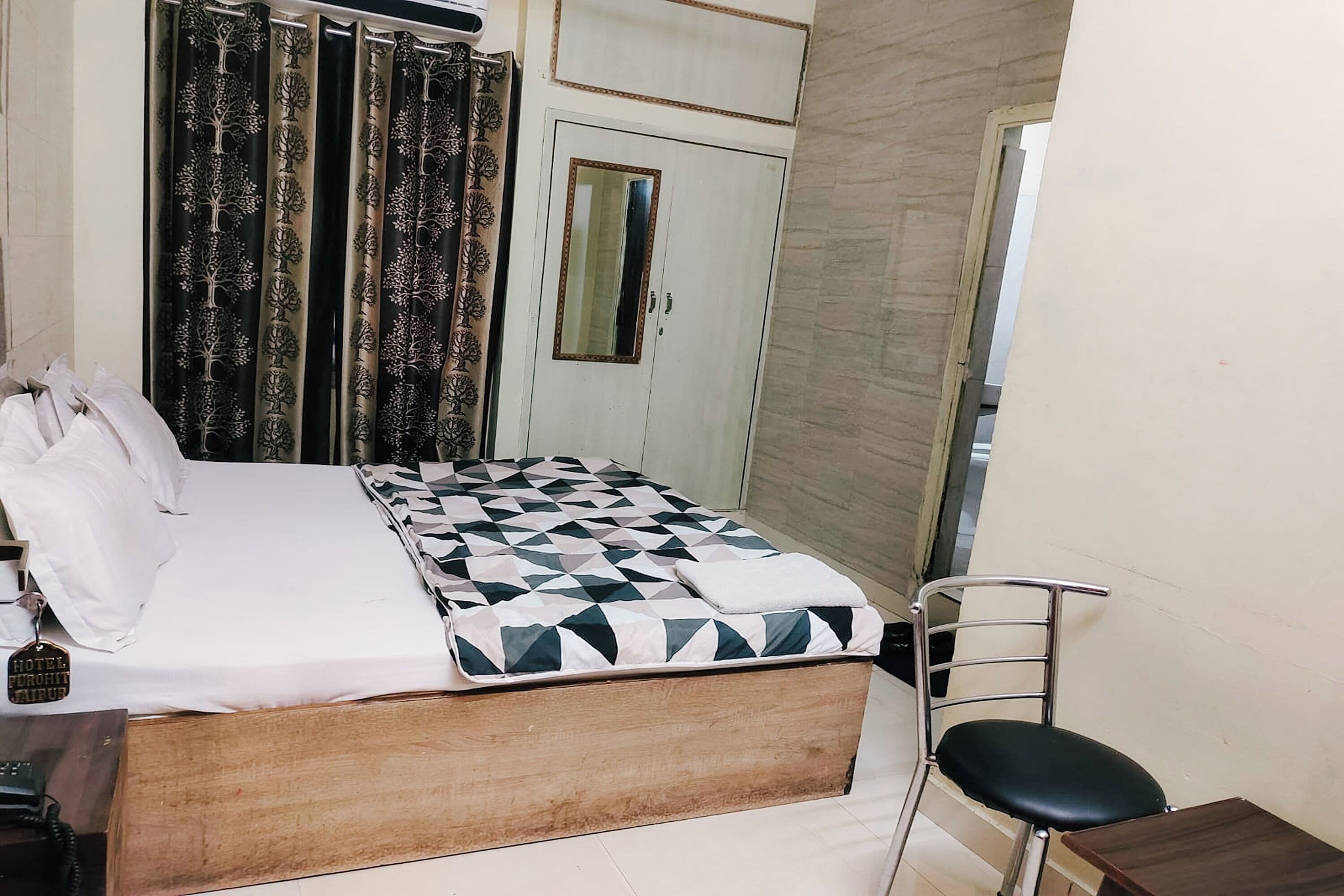 A bedroom with a bed, a chair, a small table, a wardrobe, and curtains.