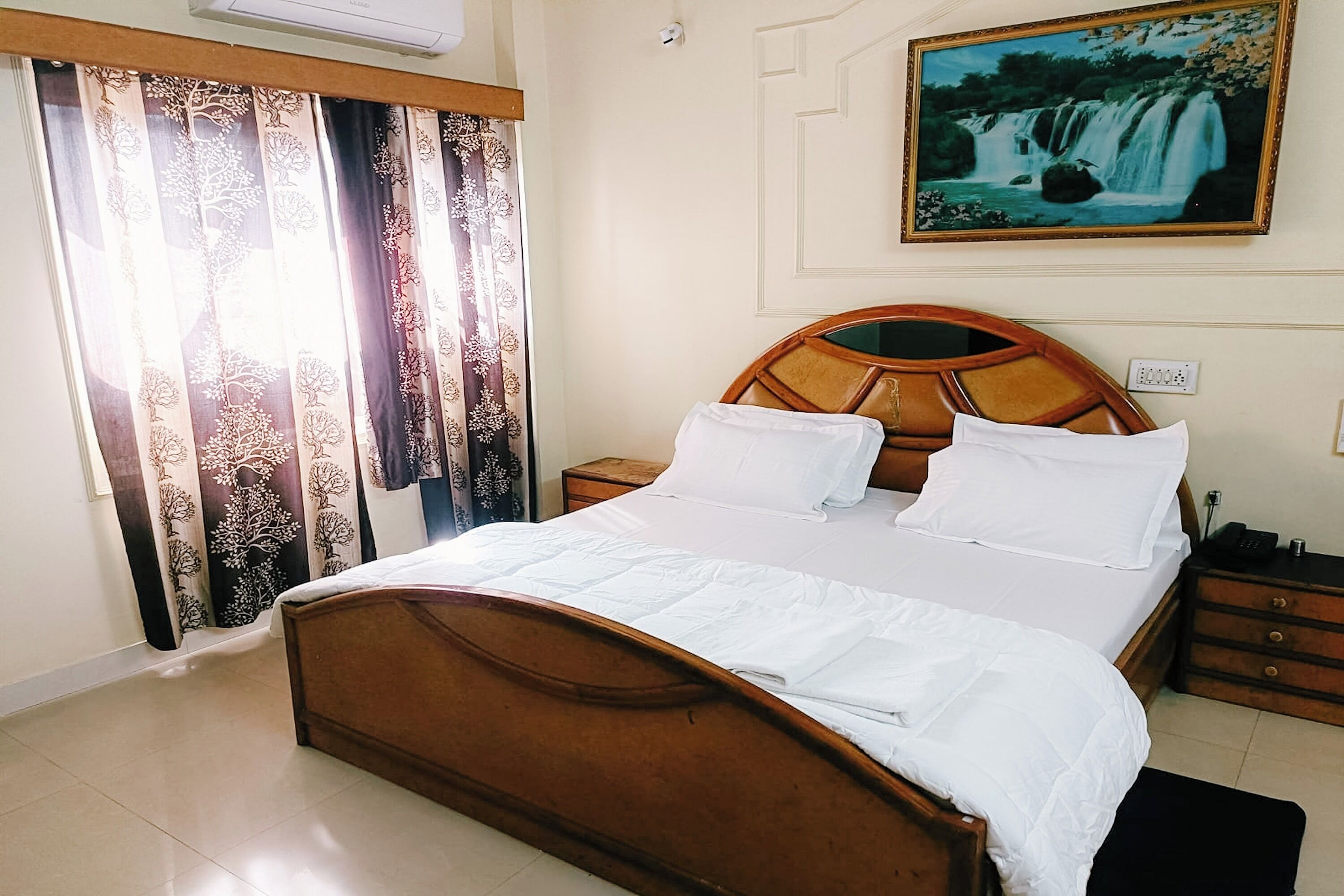 A neatly made bed with white linens, a wooden headboard, and a nightstand with a lamp.